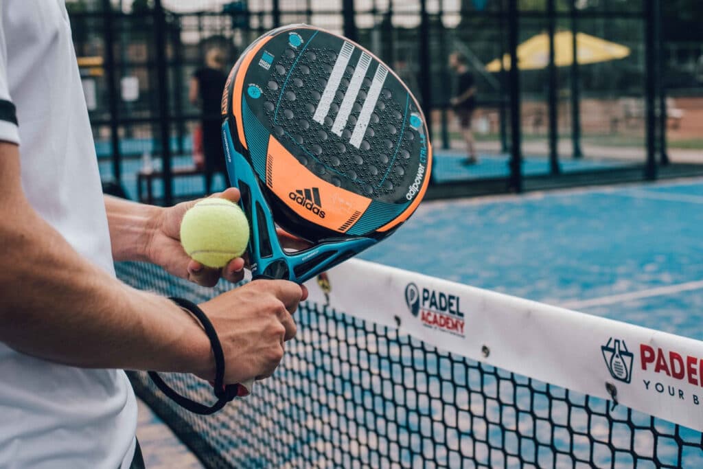 Close-up van een persoon die een padel racket vast heeft en naast een net staat