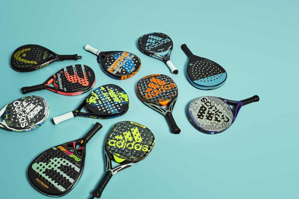 Een aantal padel rackets op de grond van verschillende merken. 