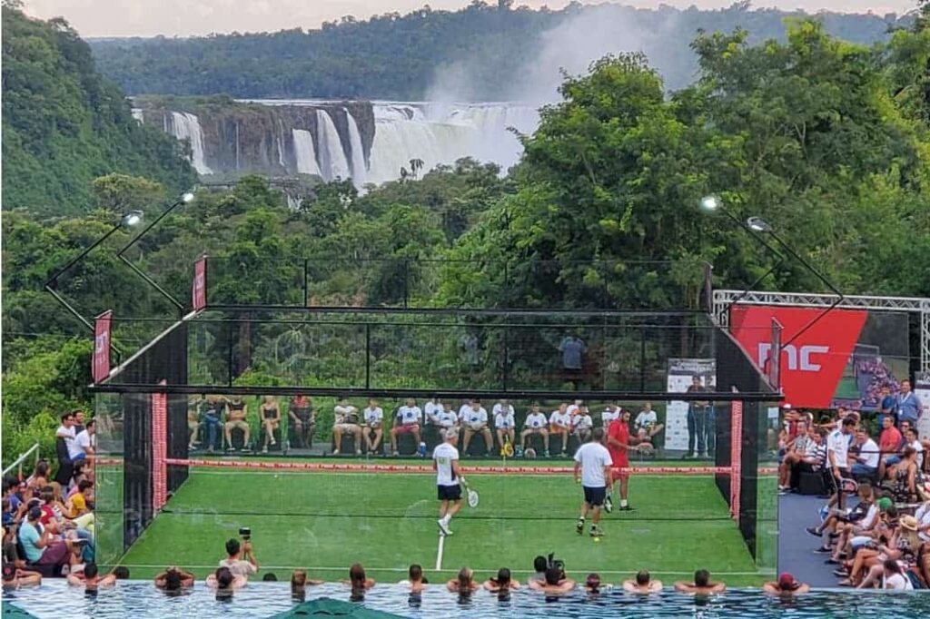Een foto van een padelbaan en veel toeschouwers tijdens een oefentoernooi met uitzicht op de watervallen van Iguazu.