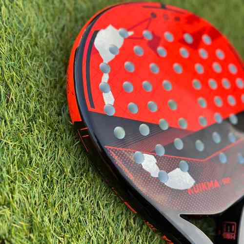 Close-up foto van een rood/zwart padel racket die lichtelijk beschadigd is. 